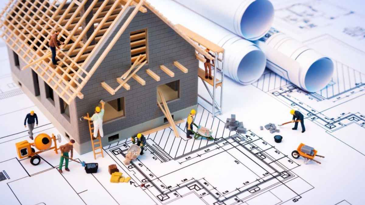 Maqueta de una vivienda en construcción con trabajadores y planos de arquitectura sobre una mesa