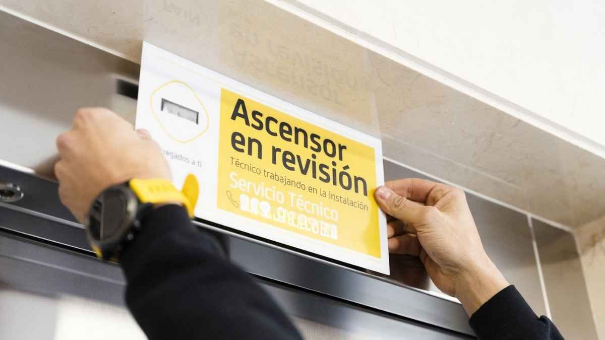 Técnico colocando un cartel de ascensor en revisión durante una inspección obligatoria