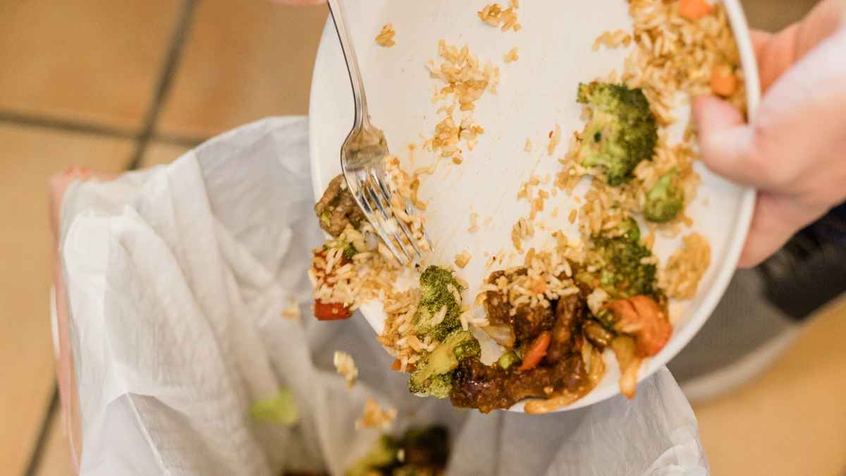 Plato con restos de comida siendo tirados a la basura en un restaurante con deficiencias de higiene.