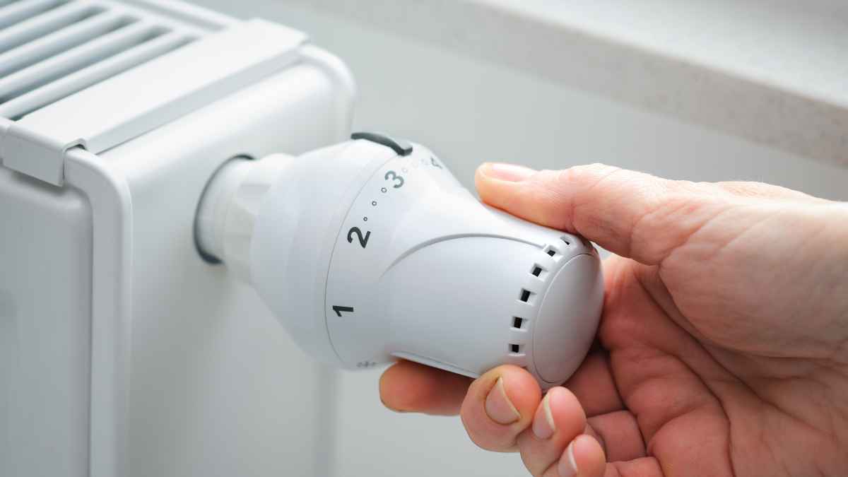 Mano ajustando el termostato de un radiador para regular la calefacción y ahorrar energía