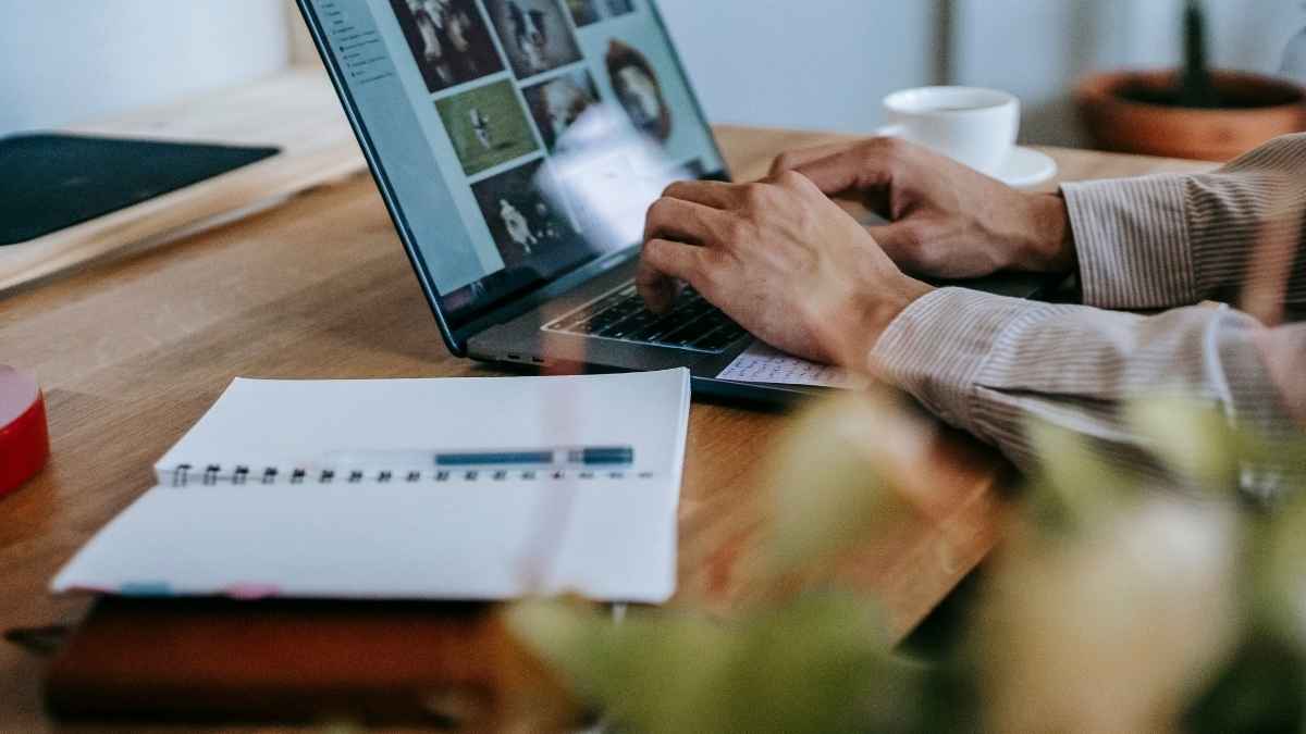 Manos trabajando en un portátil sobre un escritorio con cuaderno y taza