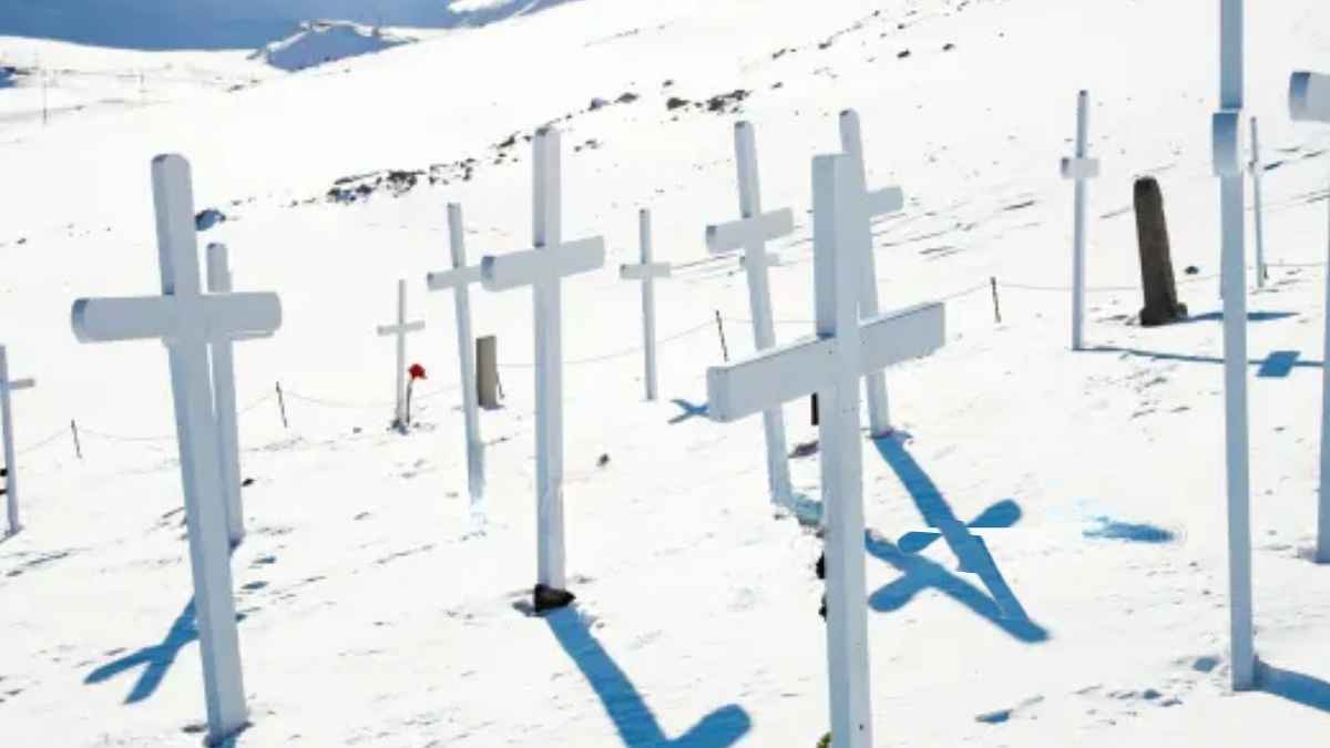 Cruces blancas en un cementerio cubierto de nieve en un paisaje ártico, con montañas al fondo.