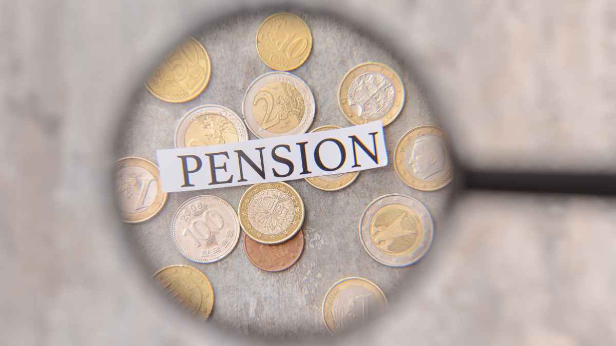 Palabra pensión enfocada con lupa sobre monedas, ilustrando el análisis fiscal de los planes de pensiones