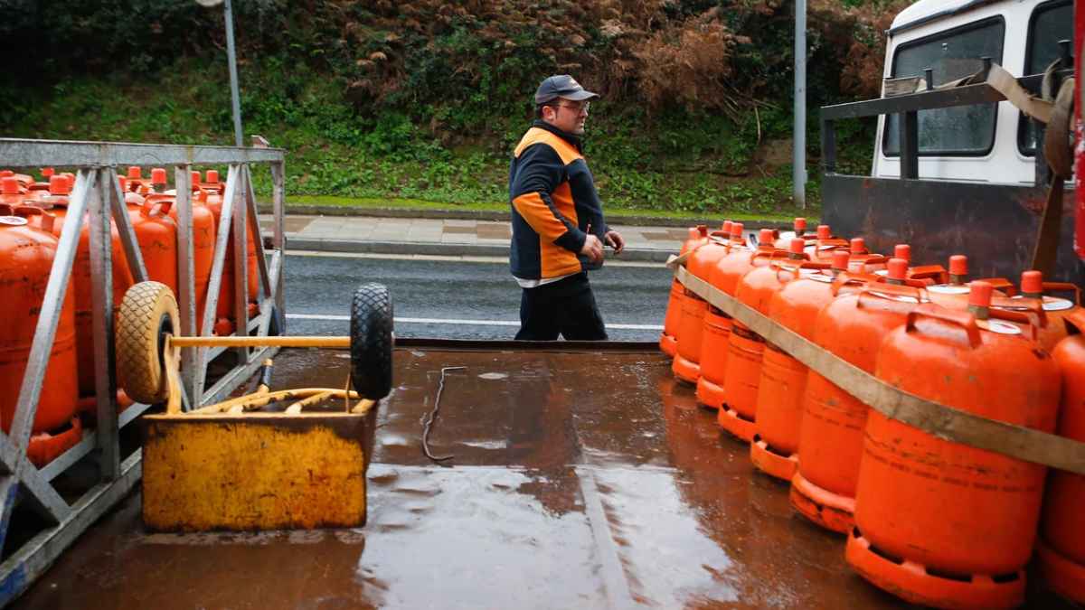 Repartidor de butano caminando junto a un camión cargado de bombonas naranjas durante su jornada de trabajo en España.