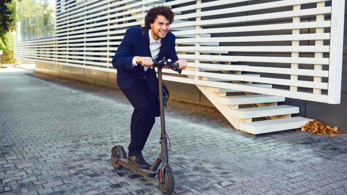 Hombre joven con traje conduciendo un patinete eléctrico en la ciudad, ilustrando la movilidad urbana y el uso de VMP