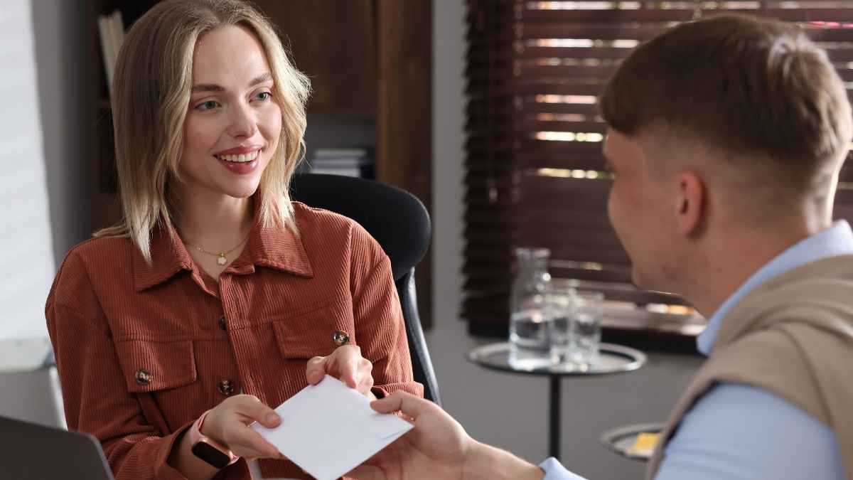 Mujer entrega un sobre de pago a un trabajador en una oficina, imagen sobre el cobro de la nómina en efectivo.