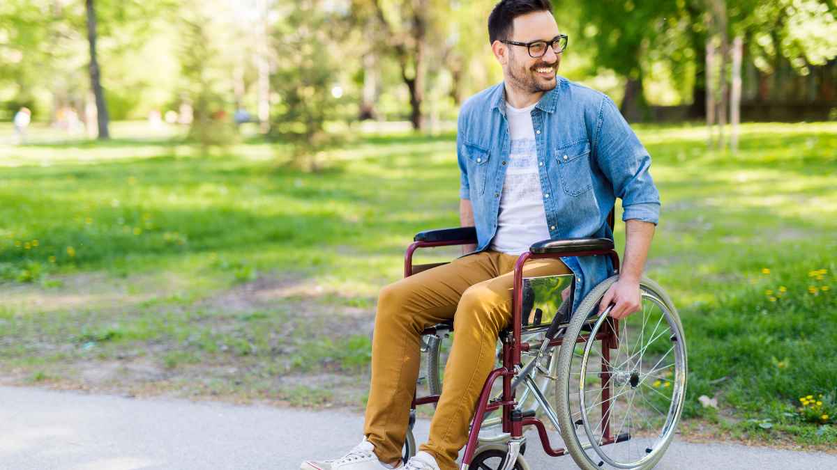 Trabajador en silla de ruedas sonriente en un parque tras adaptación laboral por incapacidad
