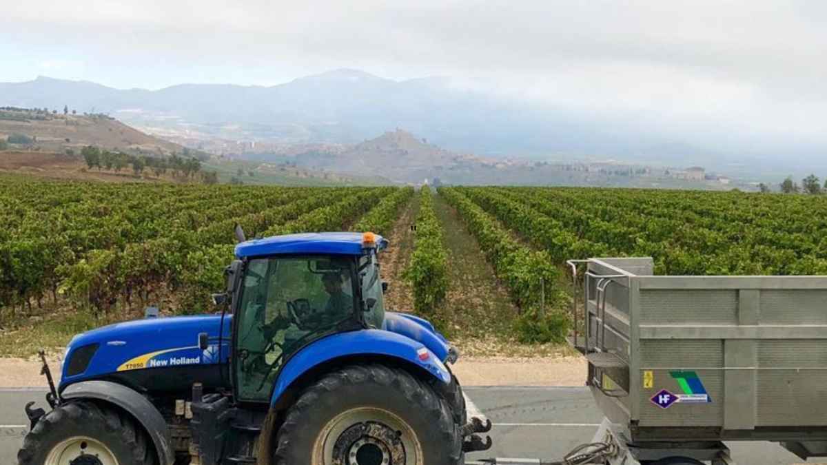 Tractor azul con remolque junto a viñedos en La Rioja