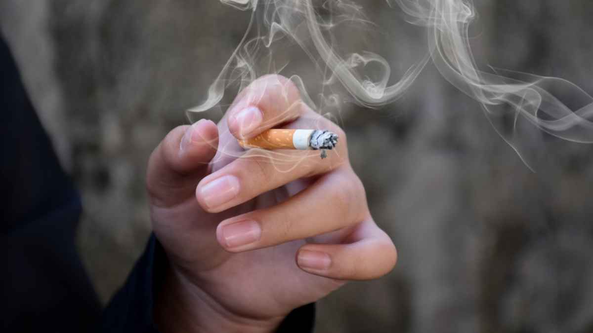 Mano sosteniendo un cigarrillo encendido con humo en primer plano, imagen ilustrativa sobre dejar de fumar con ayuda de la Seguridad Social