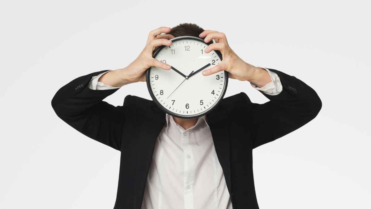 Trabajador con traje sujetando un reloj grande simbolizando la puntualidad en la jornada y el riesgo de despido según la ley laboral