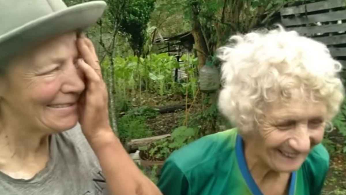 Dos hermanas mayores sonríen en su huerta en el bosque de Brasil, donde viven de forma autosuficiente y sin desperdicio.