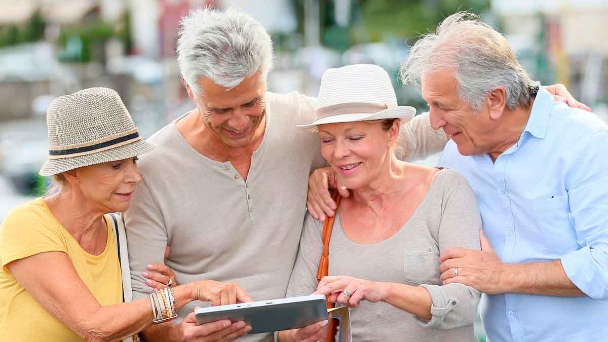 Grupo de personas mayores de 55 años interactuando con una tablet, destacando el uso de la tecnología en la tercera edad