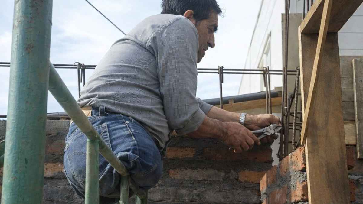 Trabajador de la construcción sobre andamio reforzando hierro en un muro de ladrillo