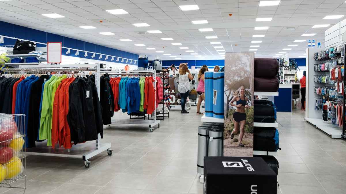 Interior de una tienda de ropa y material deportivo con percheros, accesorios y productos de varias marcas
