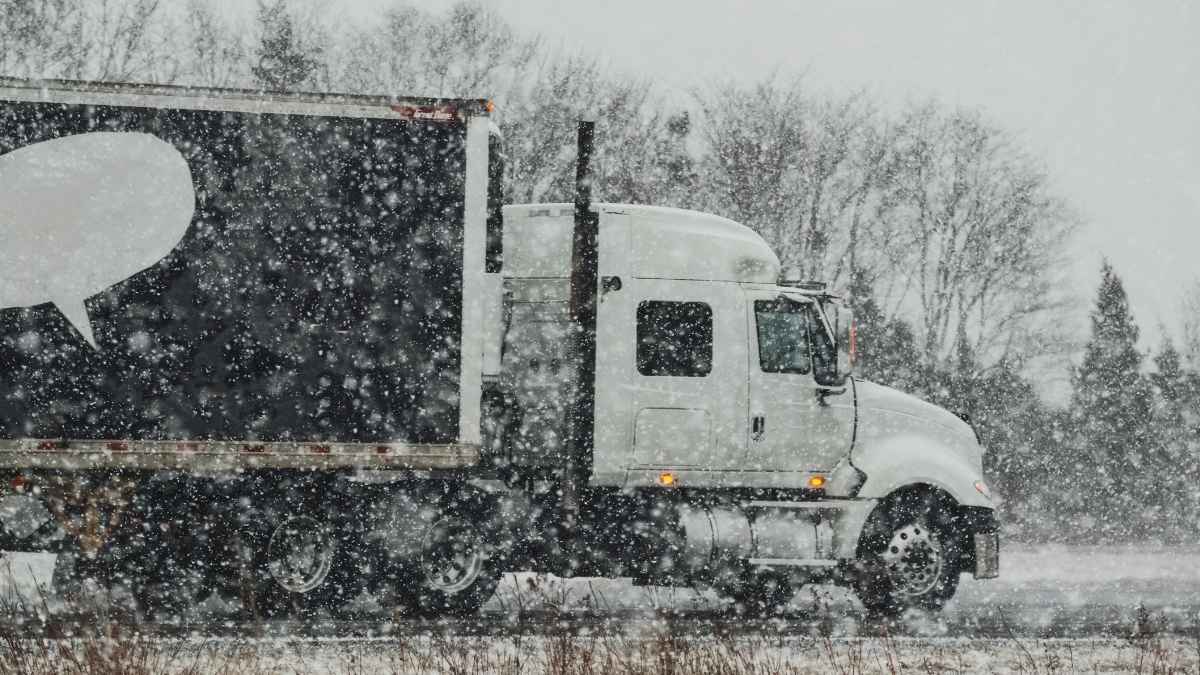 Camión de transporte circulando por carretera con nieve intensa y baja visibilidad.