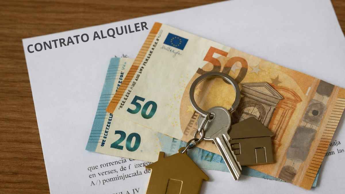 billetes de 50 y 20 euros, llaves con llavero en forma de casa y contrato de alquiler sobre mesa de madera