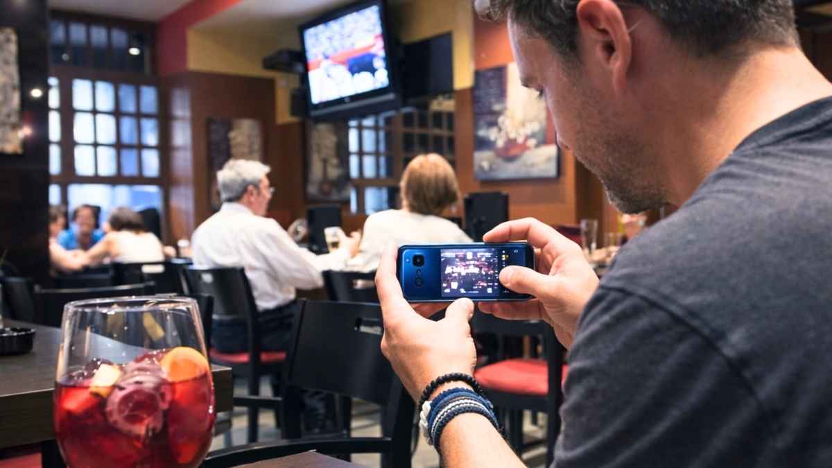 Hombre en un bar utilizando su teléfono móvil mientras clientes consumen en un restaurante de hostelería