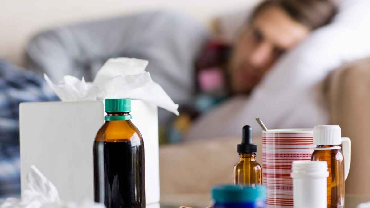 Medicamentos y pañuelos sobre una mesa mientras un trabajador permanece de baja en la cama