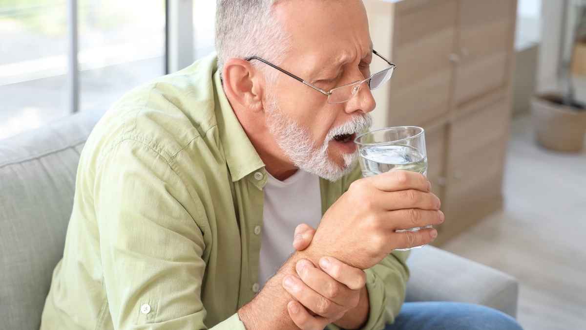 Hombre mayor con temblor en la mano sostiene un vaso de agua en casa en una imagen sobre incapacidad permanente y jubilación
