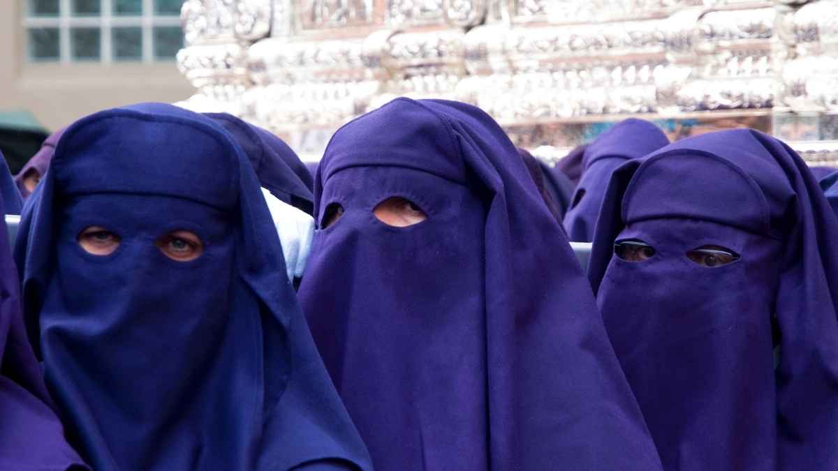 Grupo de mujeres con túnicas moradas participando en una procesión religiosa con el rostro cubierto