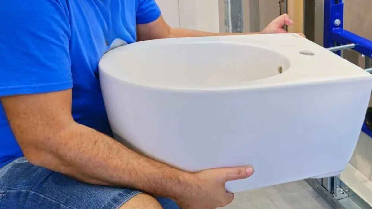 Un hombre sostiene un bidet blanco durante su instalación en un baño de una vivienda nueva en España
