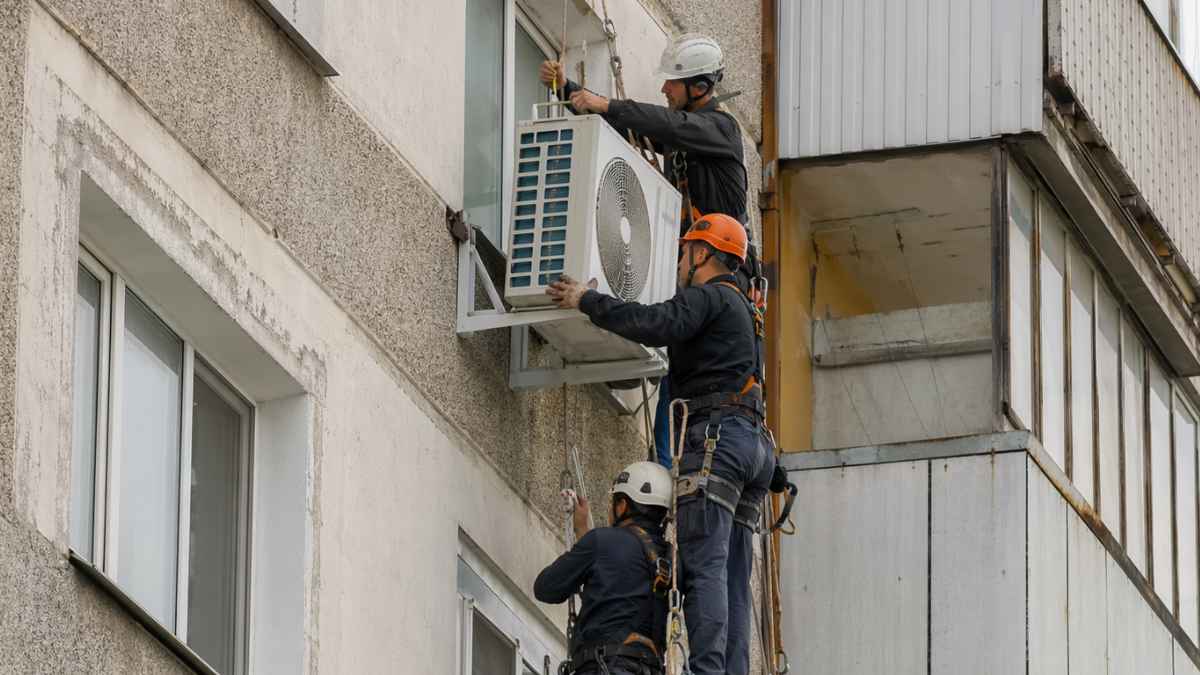 Técnicos instalan un aparato de aire acondicionado en la fachada de un bloque de pisos