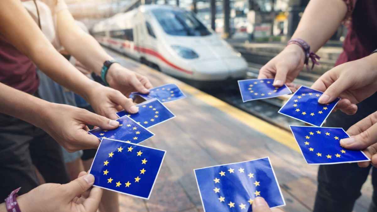 Jóvenes con tarjetas de la Unión Europea en una estación junto a un tren del programa DiscoverEU