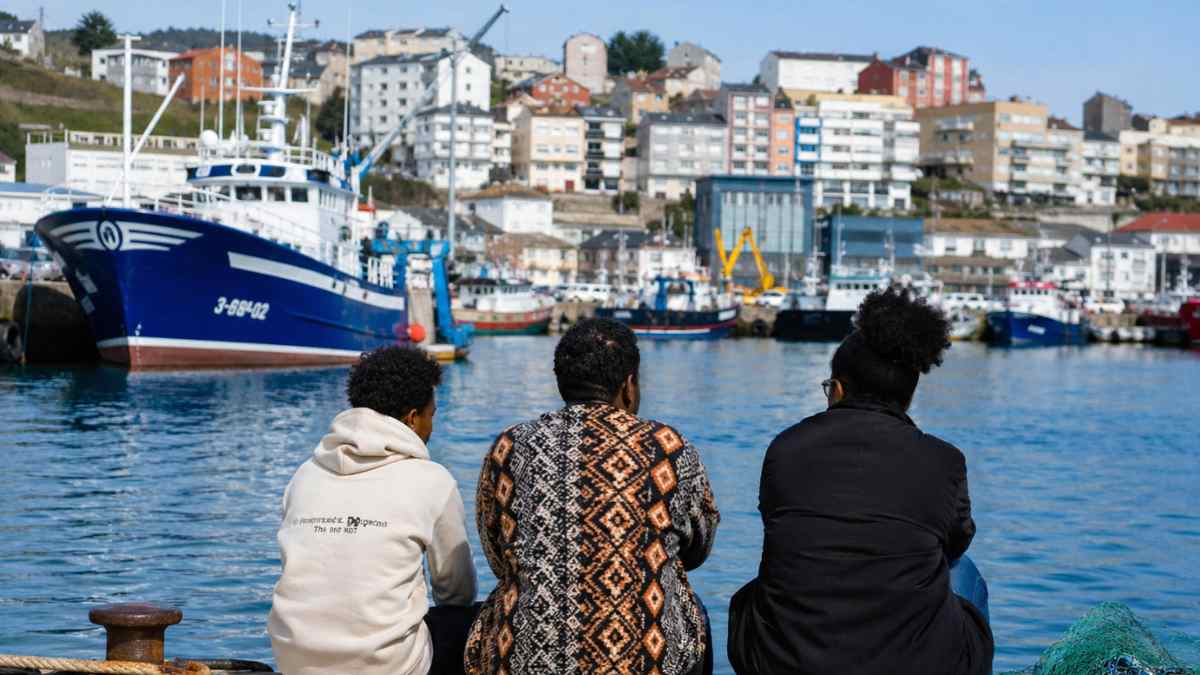 Comunidad caboverdiana en el puerto de Burela Lugo con barcos pesqueros y vecinos mirando al mar
