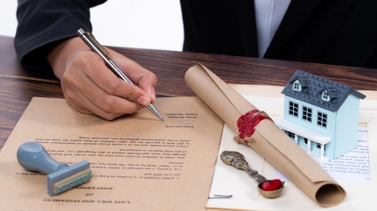 mujer firmando documentos de herencia con vivienda y testamento sobre mesa