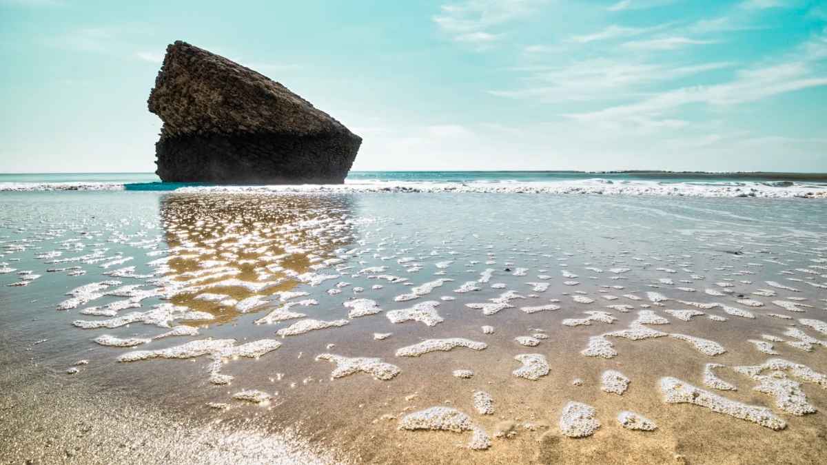 Roca en la orilla de la playa de Matalascañas con espuma del mar en primer plano