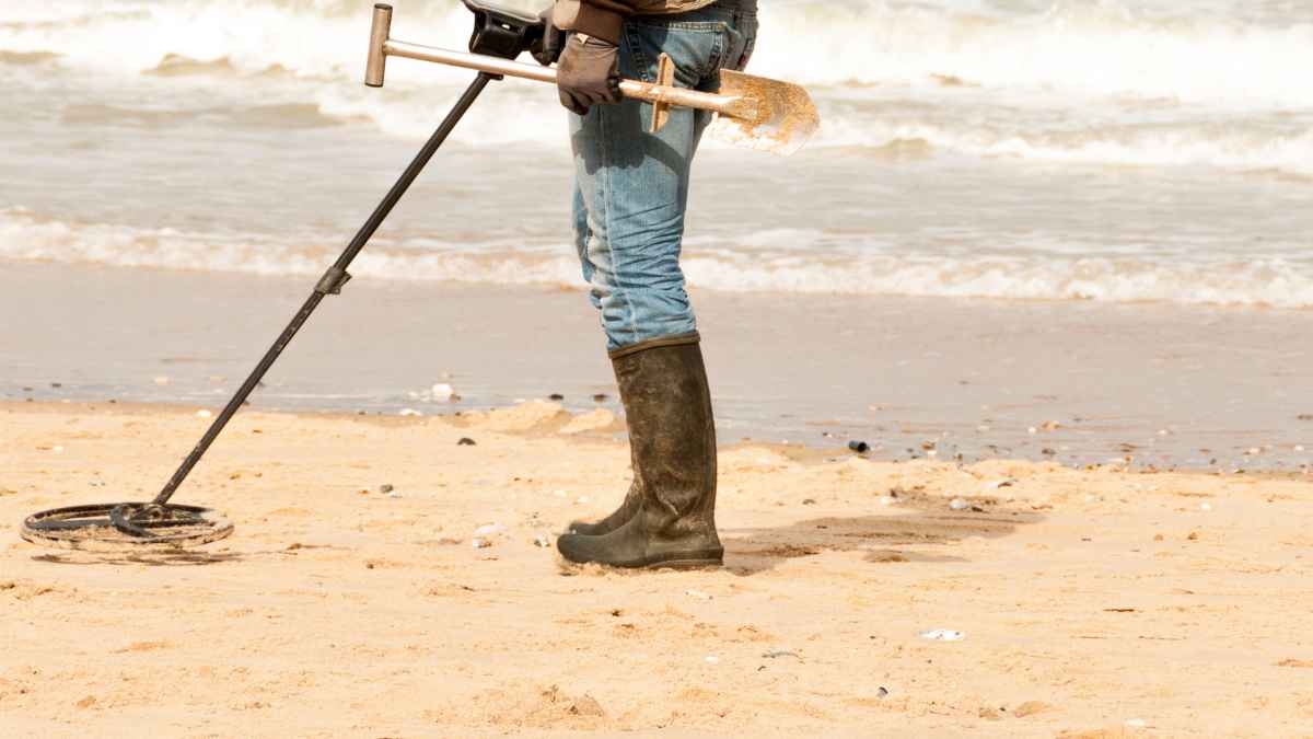 Persona usando un detector de metales en la arena de una playa junto al mar