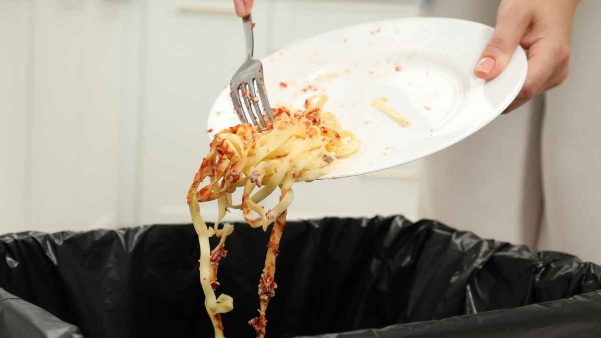Persona tirando un plato de pasta a la basura por desperdicio de comida