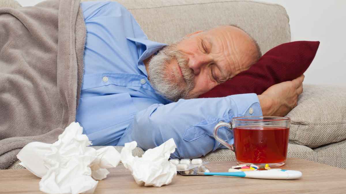 Hombre de baja médica descansando en un sofá de su casa con medicamentos, pañuelos y un termómetro