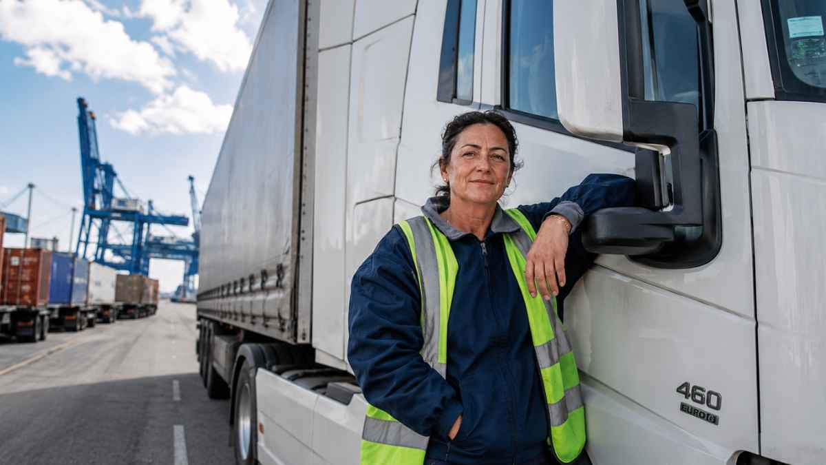 Begoña, camionera con 31 años de experiencia, posa junto a un camión en una zona portuaria con contenedores.