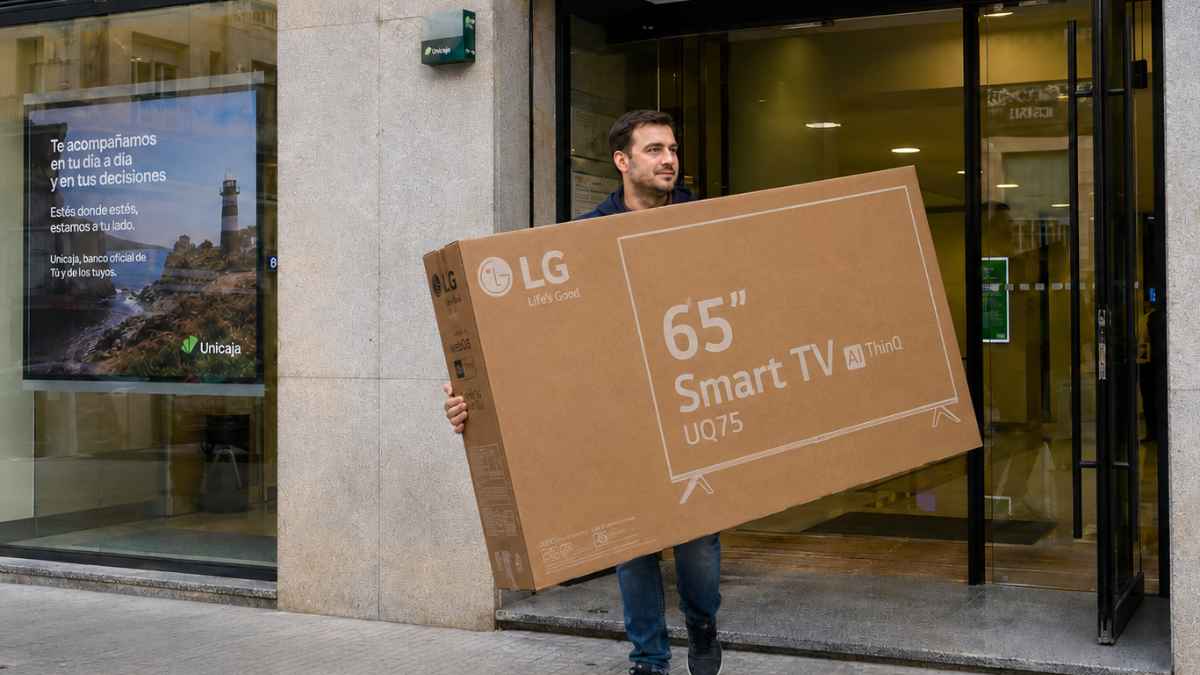 Hombre saliendo de una oficina de Unicaja con una caja de televisor LG de 65 pulgadas