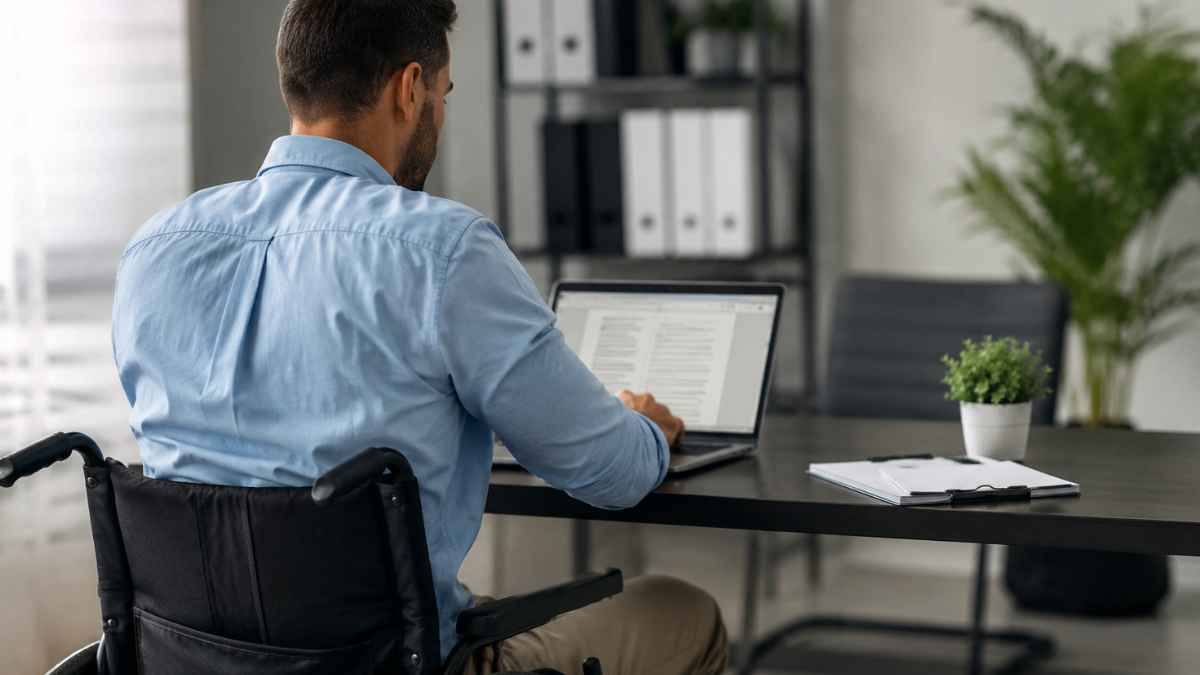 Trabajador en silla de ruedas utilizando un ordenador en una oficina tras recuperar su empleo después de un despido por incapacidad