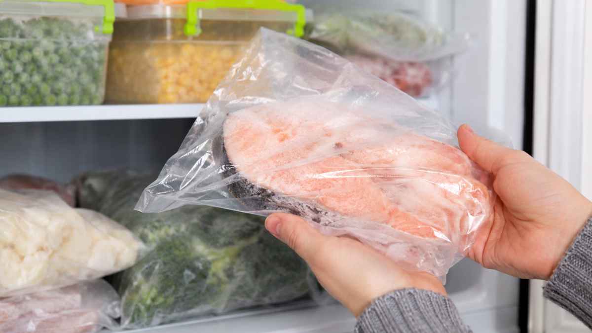 Persona sostiene pescado congelado en una bolsa de plástico dentro del congelador