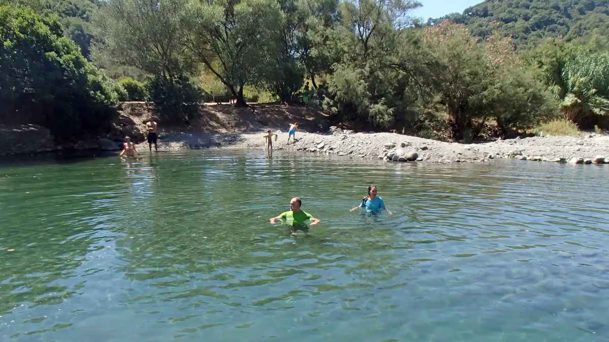 Personas bañándose en el Charco de la Escribana, una piscina natural del río Genal en Málaga rodeada de árboles