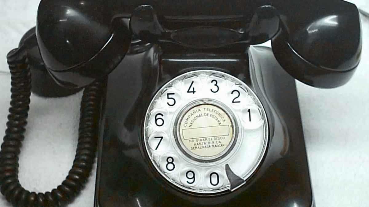 Teléfono fijo antiguo de disco negro colocado sobre una superficie blanca