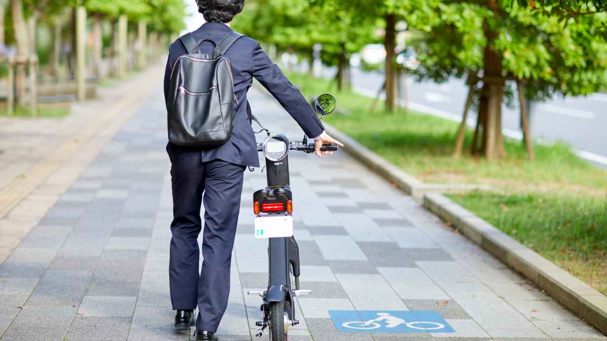 Hombre caminando con un patinete eléctrico por un carril bici para solicitar ayudas de movilidad personal