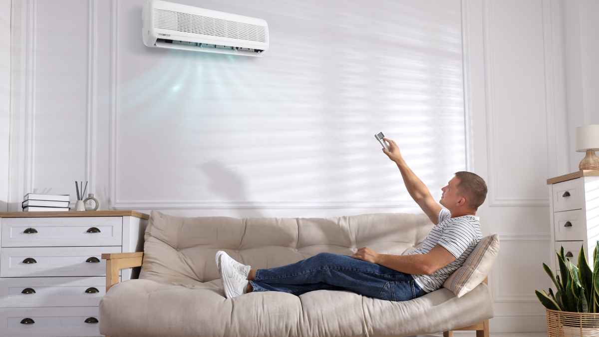 Hombre sentado en un sofá utilizando un aire acondicionado en casa durante el verano para combatir el calor.