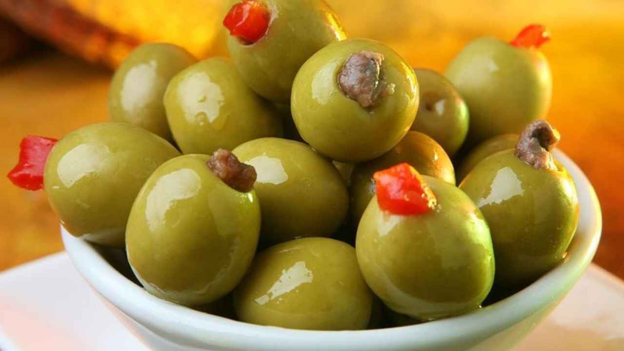 Tarros de aceitunas rellenas y pepinos en vinagre junto a etiquetas de producto en un supermercado.