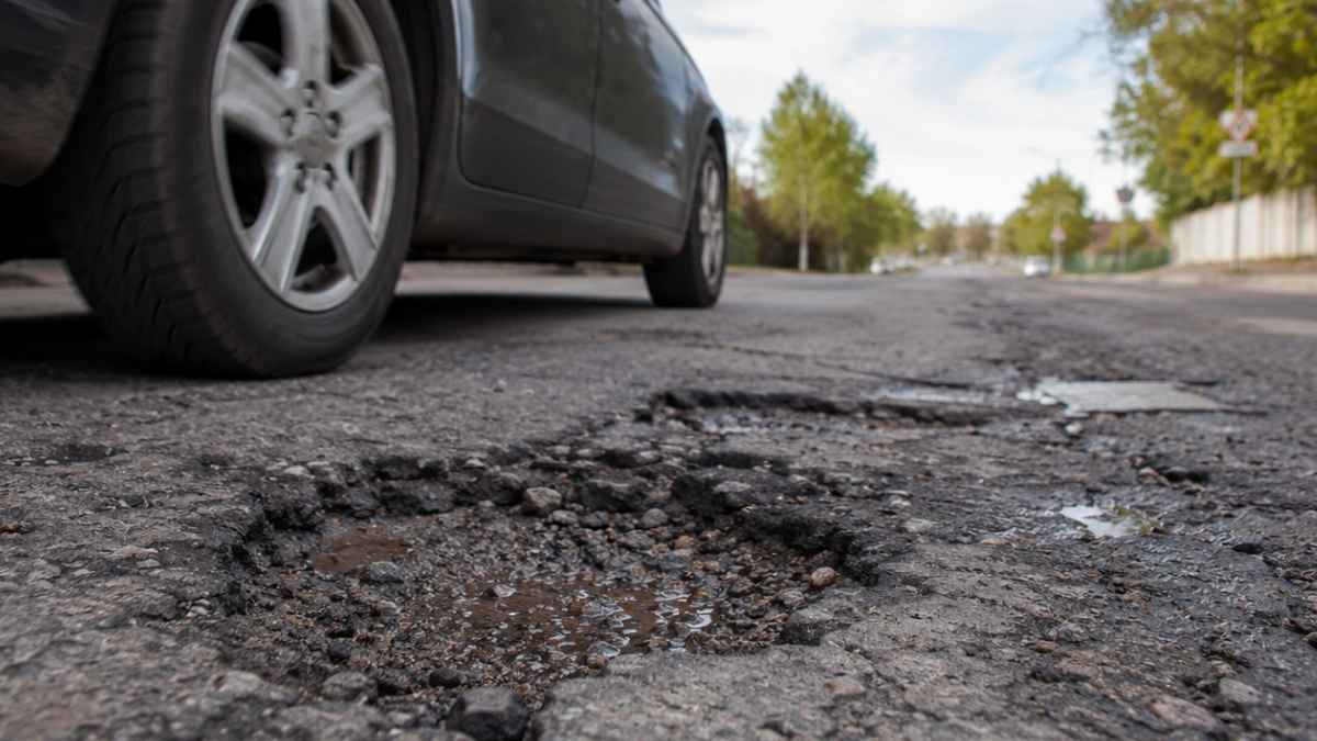 Coche pasando junto a un bache en una carretera deteriorada que puede provocar daños en la suspensión y en la electrónica del vehículo.