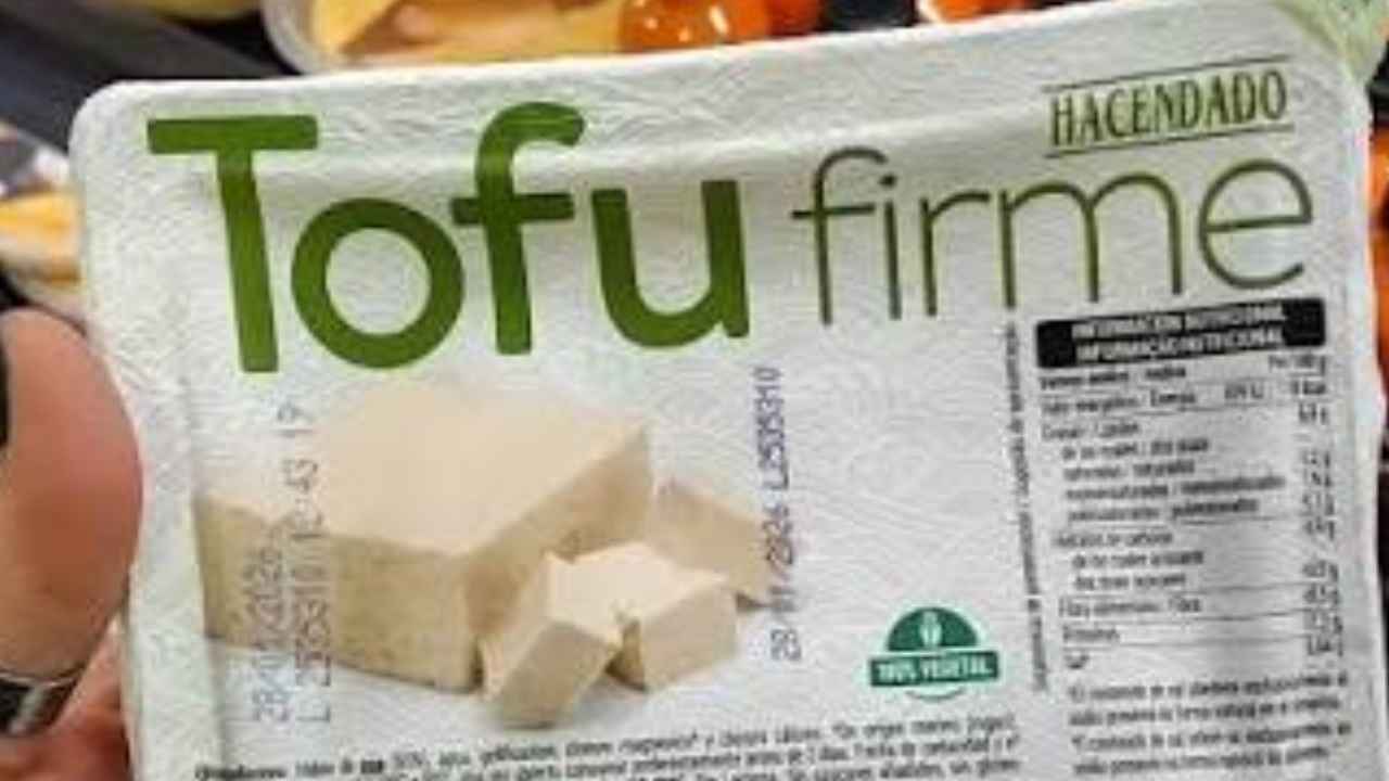 Envase vacío de tofu reutilizado como organizador dentro de un armario de cocina.