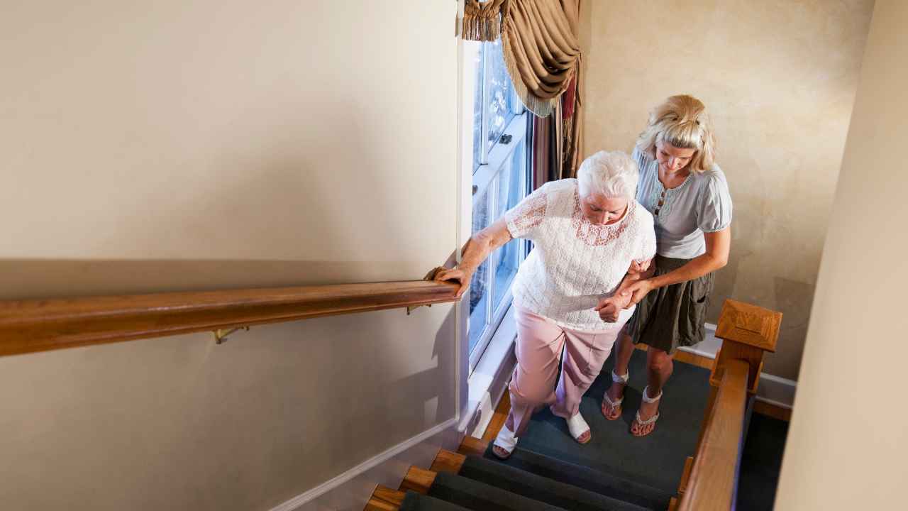 Mujer mayor subiendo las escaleras de su casa apoyado en el pasamanos.