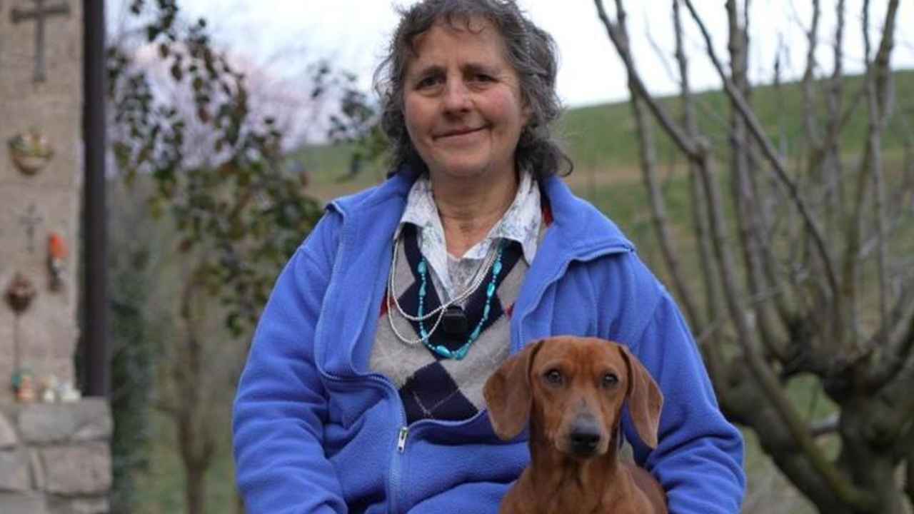 Mujer con chaqueta azul sentada junto a un perro en una zona rural de montaña.