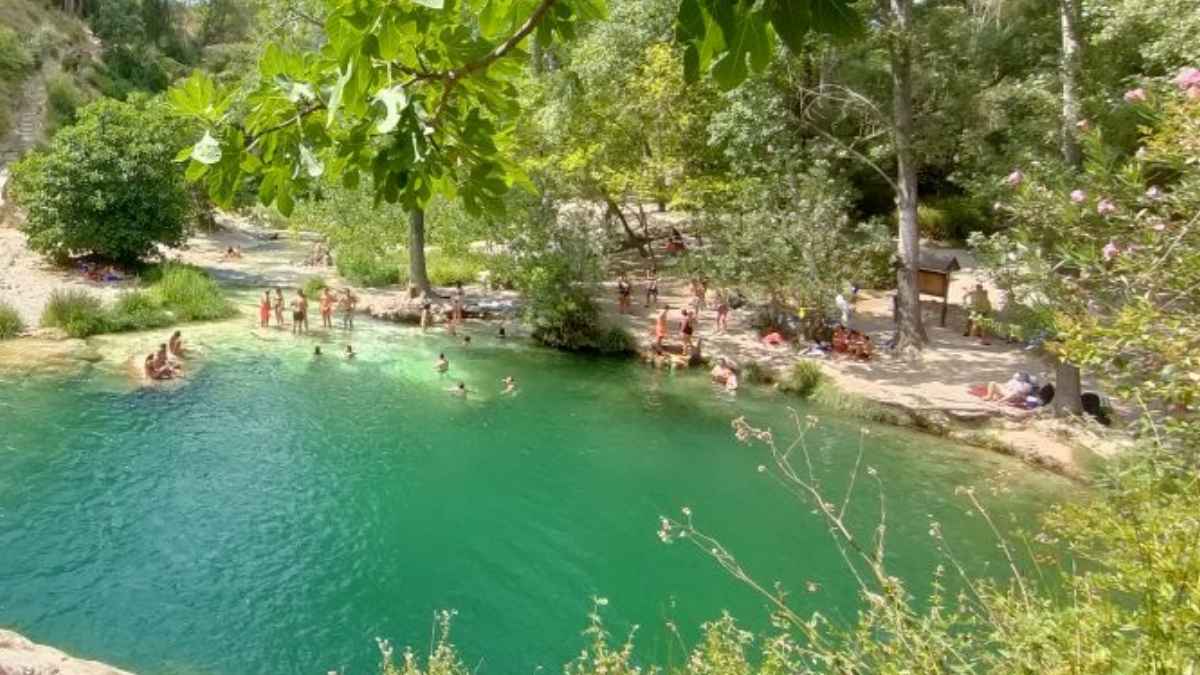 Zona de baño natural con aguas turquesas rodeada de árboles en un paraje de Valencia durante el verano.