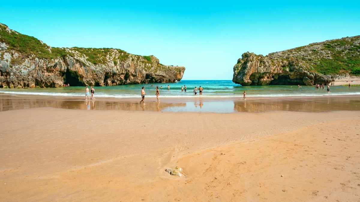 Playa del norte de España con arena dorada, aguas tranquilas y acantilados en un día de verano.