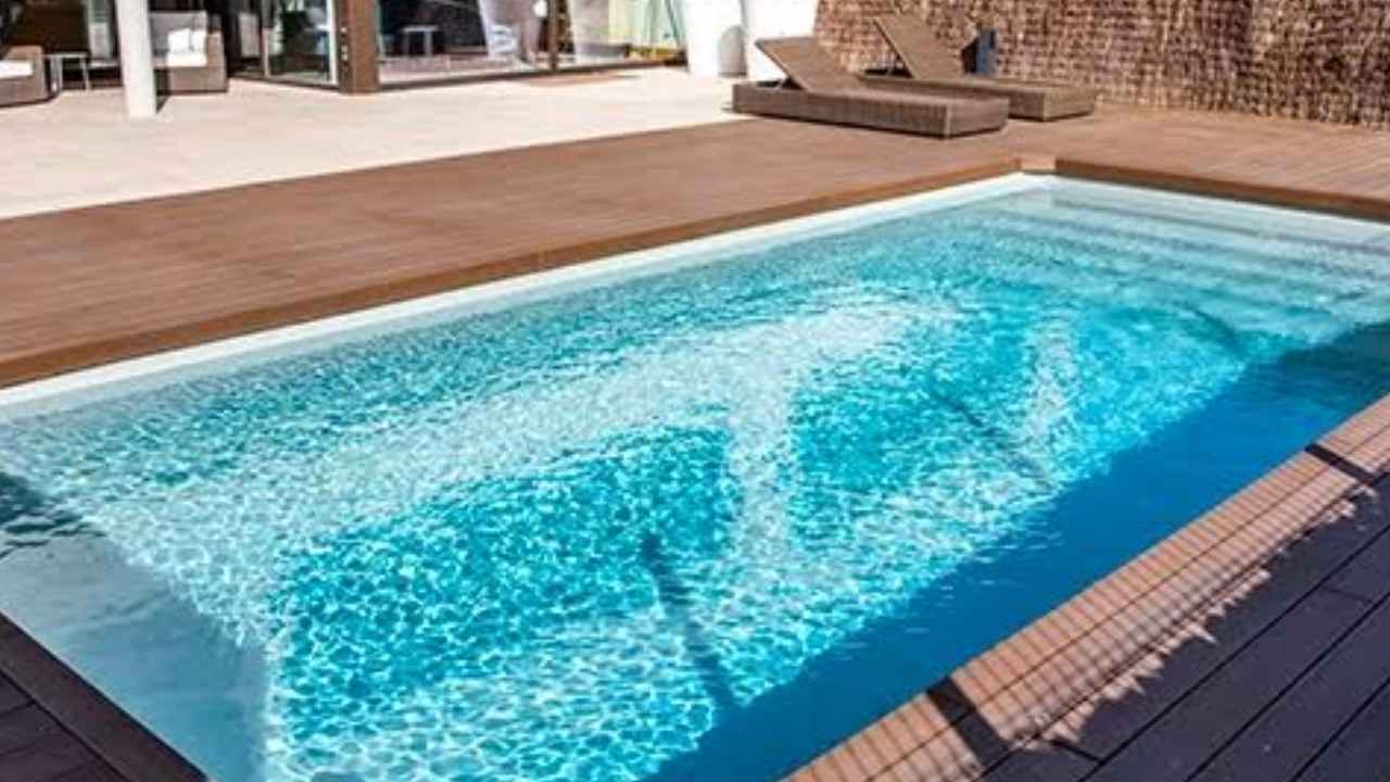 Piscina exterior de una vivienda con agua limpia y zona de madera