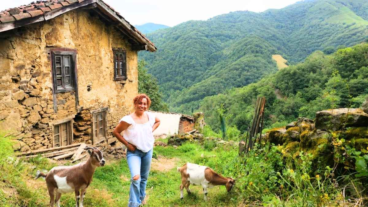 Mónica junto a dos cabras delante de una casa tradicional en una aldea de Asturias donde vive con solo ocho familias
